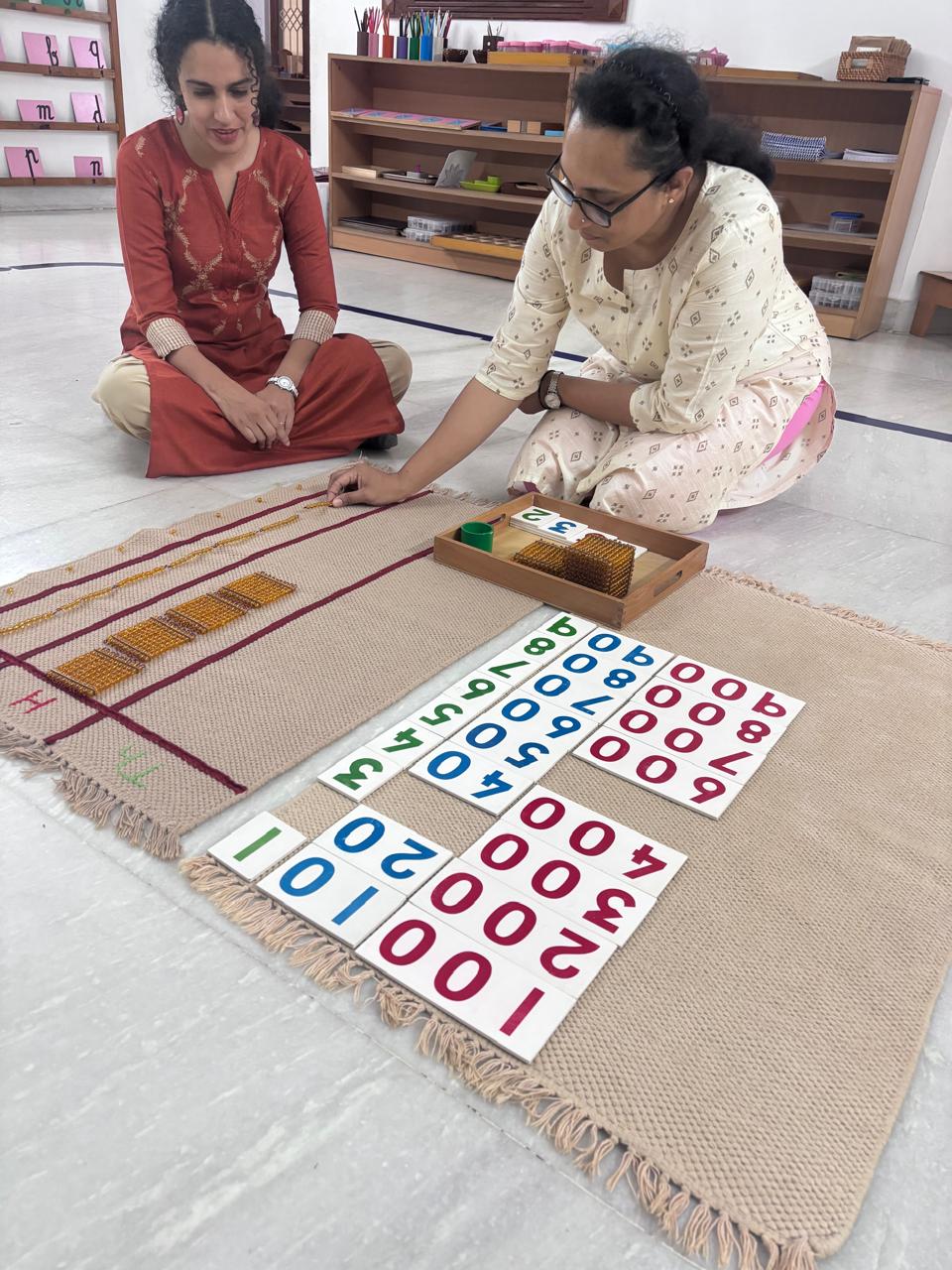 FTTA trainees working with number cards and rods on a classroom floor mat