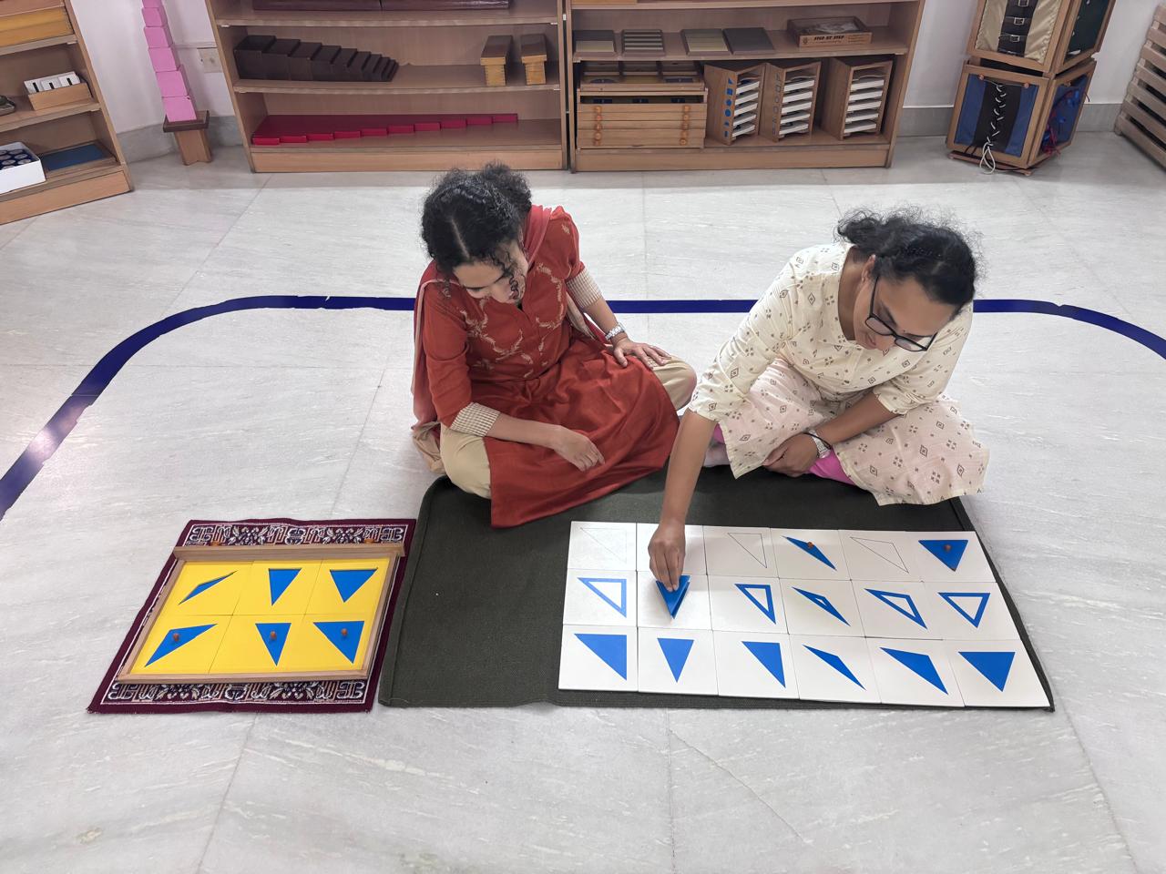 Two FTTA trainees arranging blue triangle Montessori materials on a floor mat